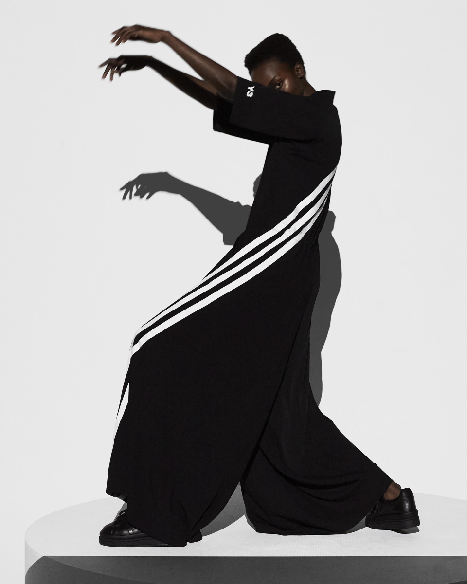 Left side view of a person in a black jumpsuit with voluminous legs that have white stripes.