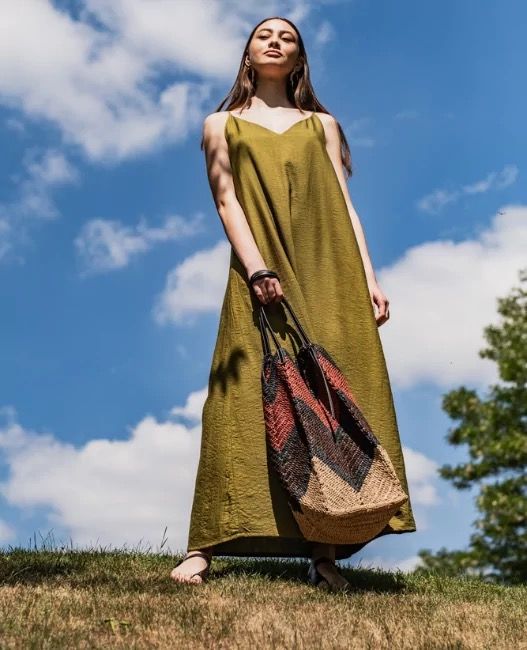 Woman wearing a slip dress in a textured olive green fabric which is fitted at the shoulders with short spaghetti straps, extending into a deep vneck at the front.