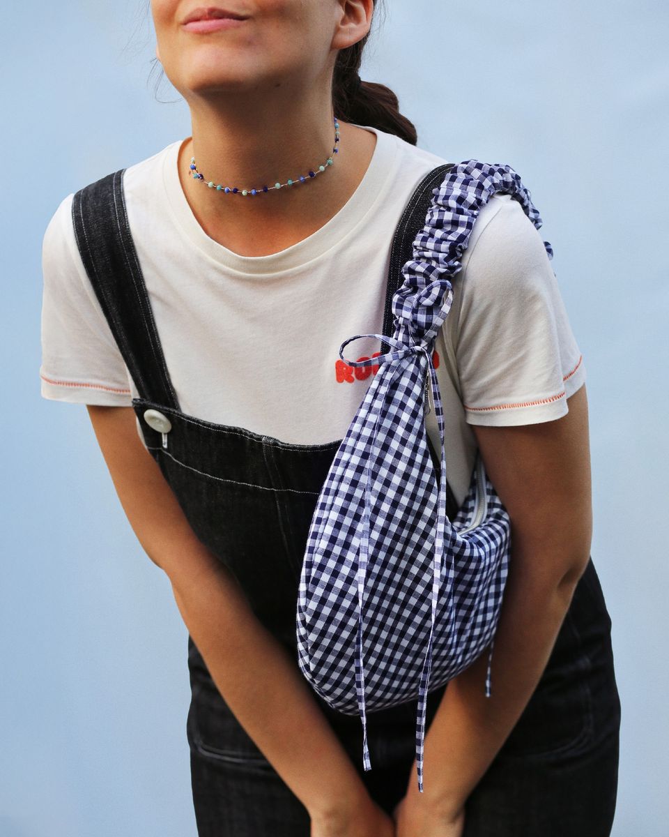 A model is wearing the Drawstring Crescent Bag with the short scrunched up strap on her left shoulder. The ties are tied into bows. The bag is made from a gingham cotton. This bag can be made with the PDF sewing pattern and video tutorial.