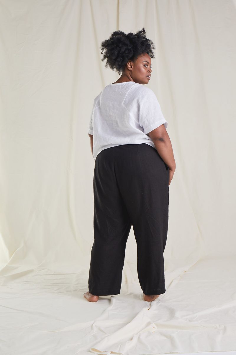 Full body back shot of model wearing top made in white fabric and black trousers