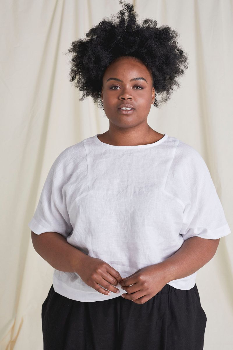 Front shot of model wearing top made in white fabric with crossed arms
