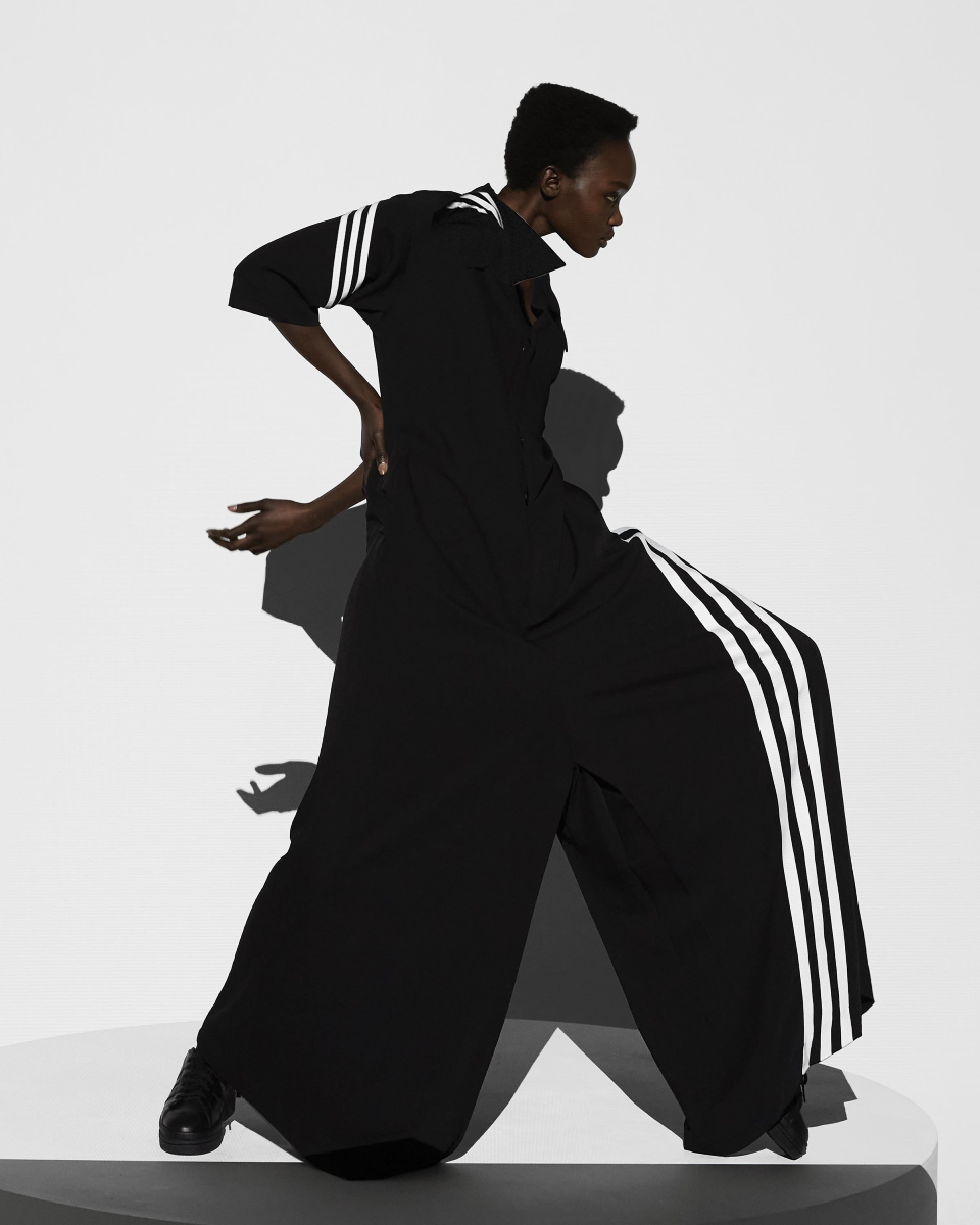 Right side view of a person in a black jumpsuit with voluminous legs that have white stripes.