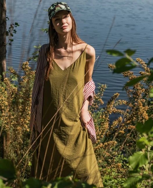 Woman wearing a loose shirt over a maxi-length slip dress which is fitted at the shoulders with short spaghetti straps, extending into a deep vneck at the front.