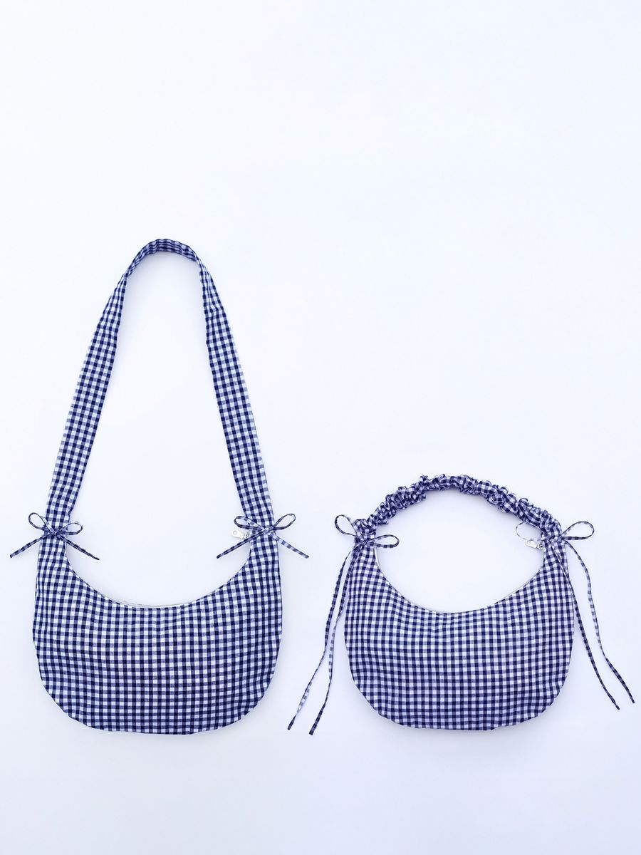 The Drawstring Crescent Bag is pictured with its long flat strap on the left, and its short scrunched up strap on the right.