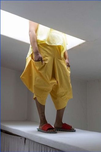 Person in yellow Leija trousers with their torso hidden by a skylight. Their hands are in their pockets.